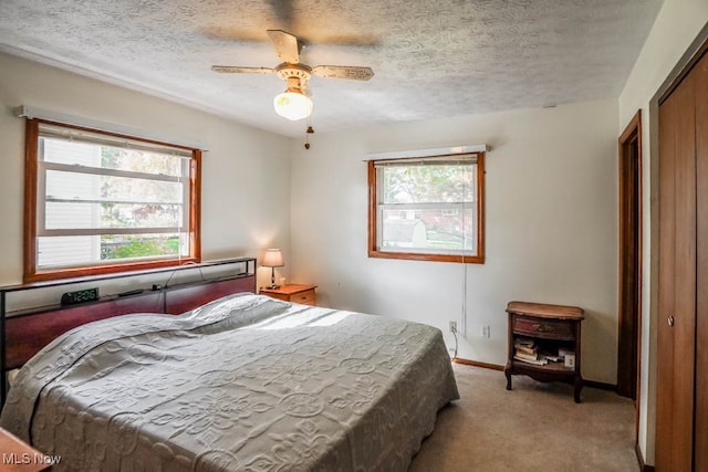 carpeted bedroom with a textured ceiling, multiple windows, ceiling fan, and a closet