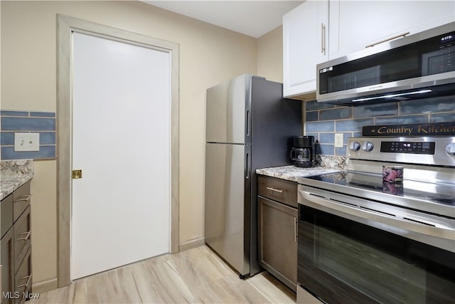 kitchen featuring light hardwood / wood-style floors, light stone counters, backsplash, white cabinetry, and appliances with stainless steel finishes