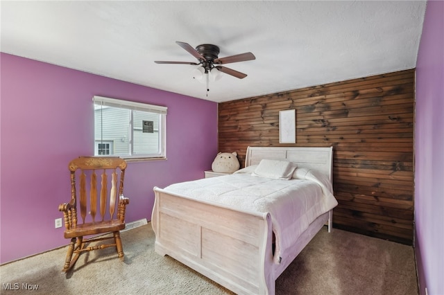 carpeted bedroom featuring wood walls and ceiling fan