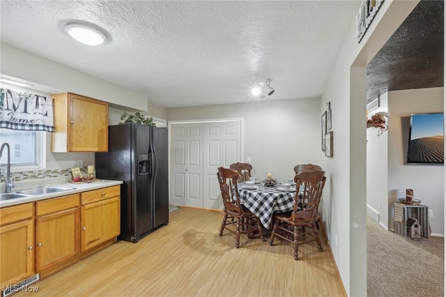 kitchen with black refrigerator with ice dispenser, light hardwood / wood-style floors, a textured ceiling, and sink