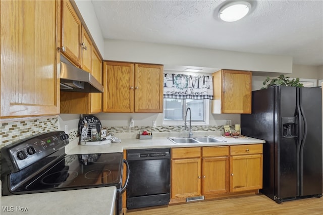 kitchen with black appliances, a textured ceiling, sink, tasteful backsplash, and light hardwood / wood-style flooring