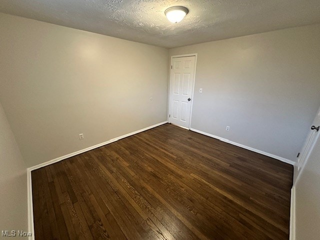 spare room featuring a textured ceiling and dark hardwood / wood-style floors