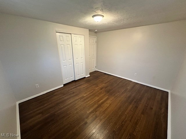 unfurnished bedroom featuring a closet, a textured ceiling, and dark hardwood / wood-style floors