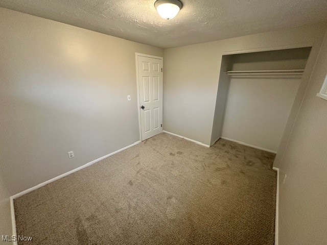 unfurnished bedroom with carpet flooring, a textured ceiling, and a closet