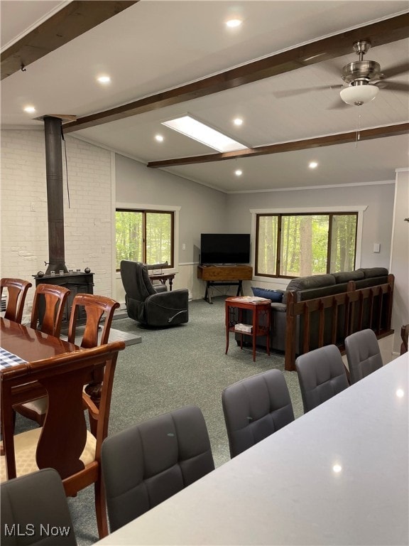 carpeted living room with ceiling fan, plenty of natural light, a wood stove, and vaulted ceiling