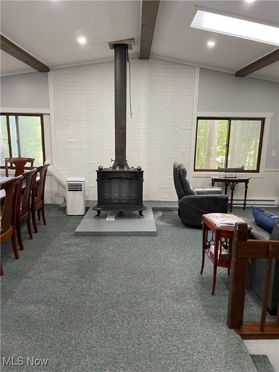 living room featuring a healthy amount of sunlight, a wood stove, vaulted ceiling with beams, and carpet floors