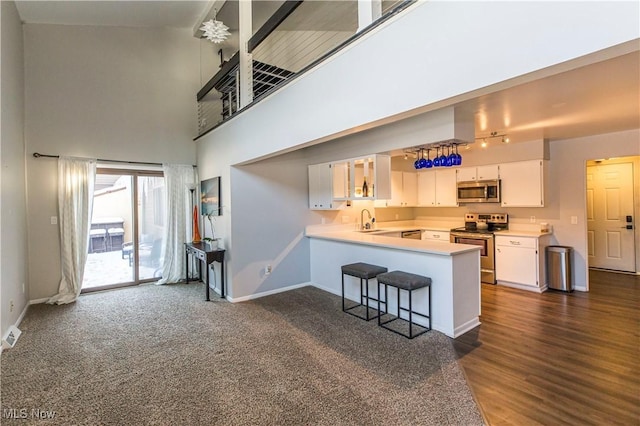 kitchen with dark carpet, appliances with stainless steel finishes, a towering ceiling, kitchen peninsula, and white cabinetry