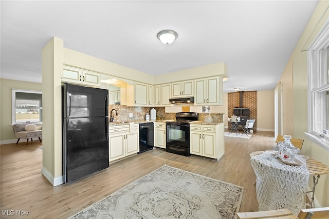 kitchen featuring black appliances, light wood-type flooring, a wood stove, and cream cabinetry