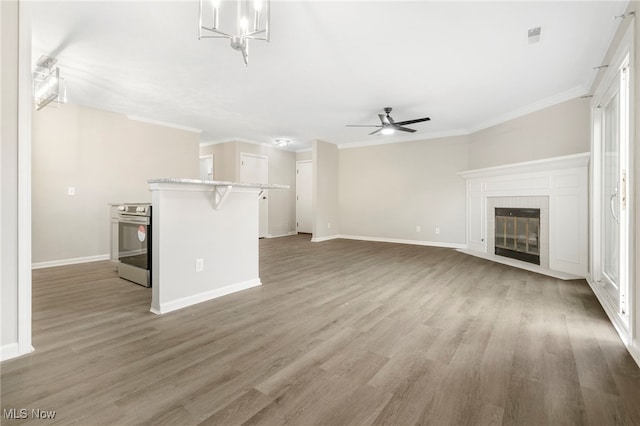 unfurnished living room with ceiling fan, a tiled fireplace, hardwood / wood-style flooring, and ornamental molding