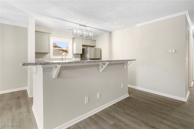 kitchen featuring dark hardwood / wood-style flooring, a textured ceiling, stainless steel fridge, and a breakfast bar