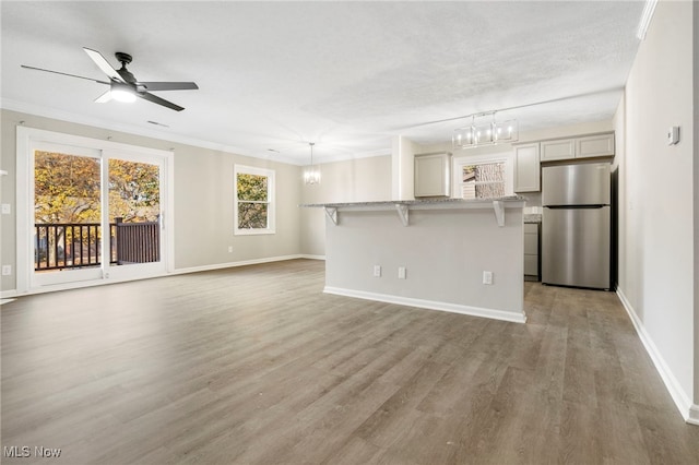 unfurnished living room with hardwood / wood-style floors, ceiling fan with notable chandelier, a textured ceiling, and crown molding