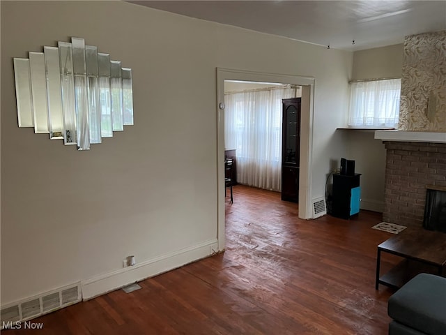 unfurnished living room featuring a brick fireplace and dark hardwood / wood-style floors