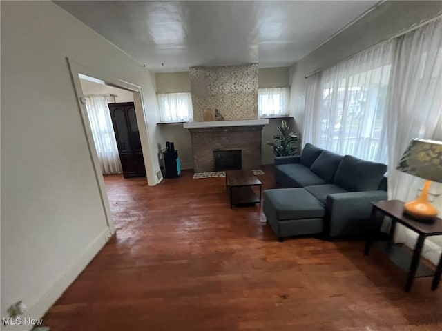 living room with dark wood-type flooring, a wealth of natural light, and a brick fireplace