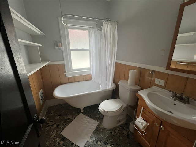 bathroom with toilet, wood walls, vanity, and a bathing tub