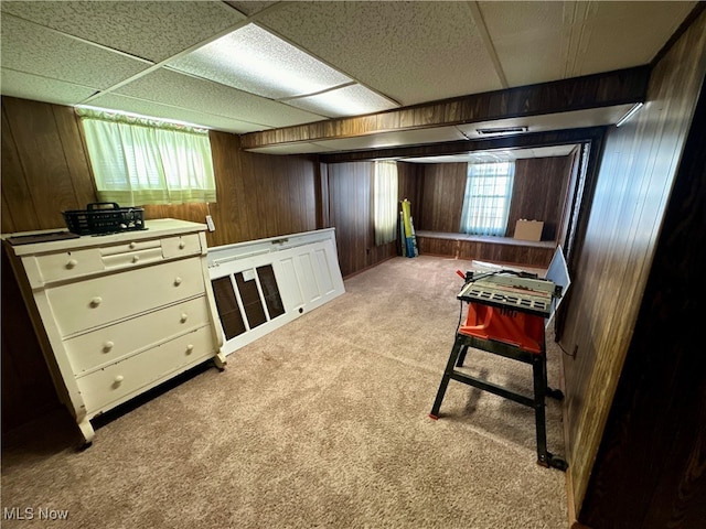 interior space featuring wood walls, light colored carpet, a healthy amount of sunlight, and a drop ceiling