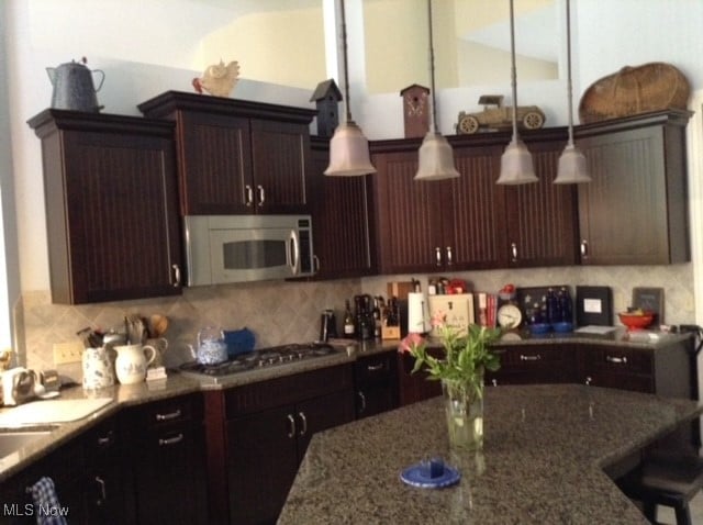 kitchen with stone countertops, appliances with stainless steel finishes, a breakfast bar area, dark brown cabinets, and decorative backsplash