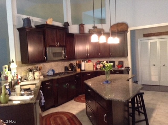 kitchen with a breakfast bar, light stone counters, decorative light fixtures, backsplash, and a kitchen island