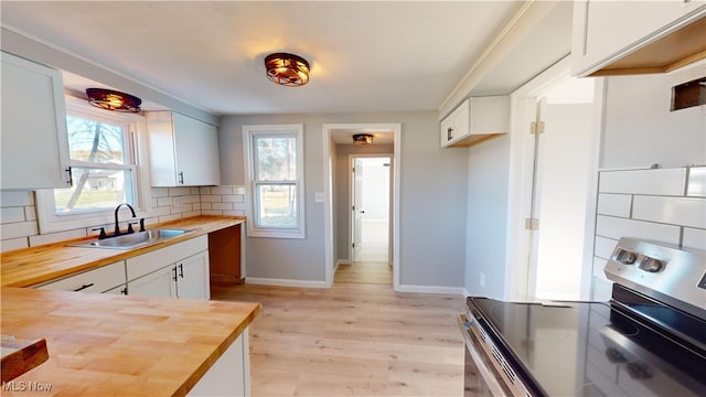 kitchen featuring butcher block countertops, tasteful backsplash, stainless steel range with electric cooktop, white cabinetry, and sink