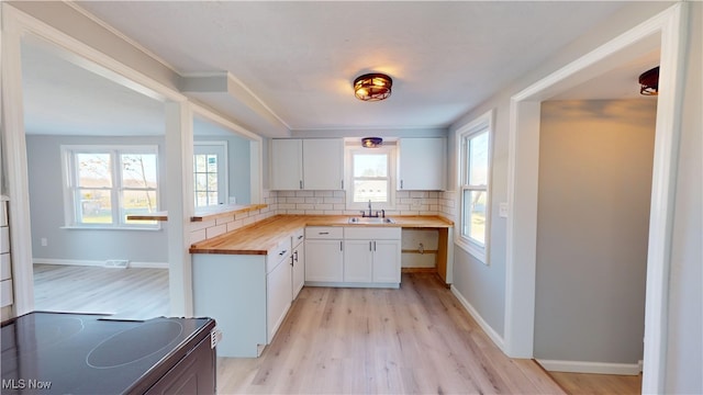 kitchen with white cabinets, sink, tasteful backsplash, butcher block countertops, and light hardwood / wood-style flooring