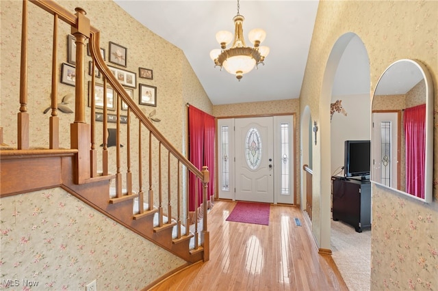 entrance foyer featuring hardwood / wood-style floors, lofted ceiling, and a notable chandelier