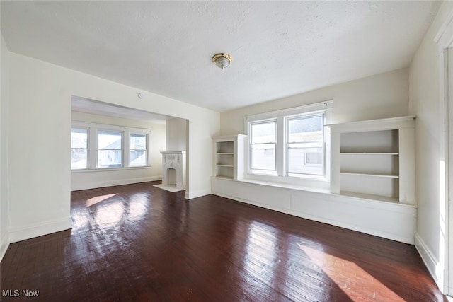 unfurnished living room with dark wood-type flooring, a wealth of natural light, and built in features