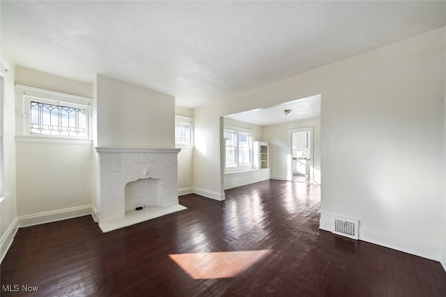 unfurnished living room with a wealth of natural light, a textured ceiling, dark hardwood / wood-style floors, and a brick fireplace