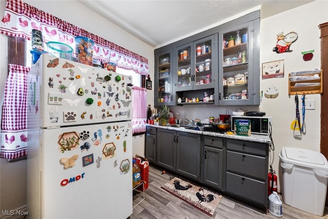 kitchen featuring light wood-type flooring, white refrigerator, and light stone countertops