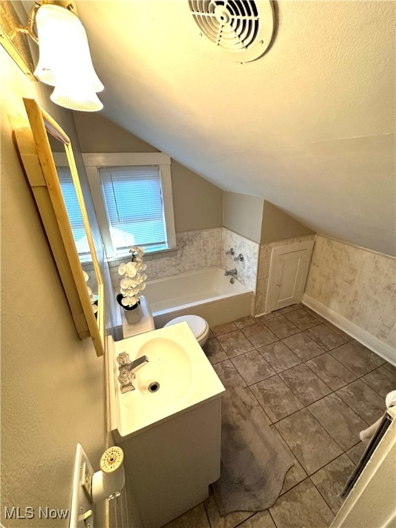 bathroom with tile patterned floors, vanity, a tub, vaulted ceiling, and toilet