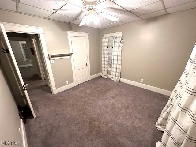 unfurnished bedroom featuring ceiling fan, dark carpet, and a drop ceiling