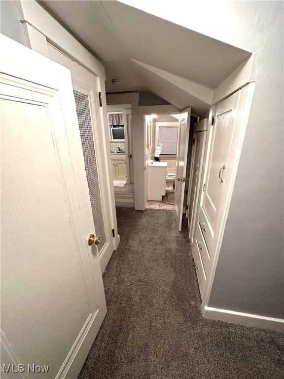 hall with dark colored carpet and vaulted ceiling