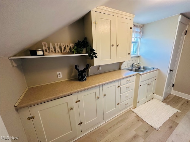 kitchen with white cabinetry, light wood-type flooring, sink, and vaulted ceiling