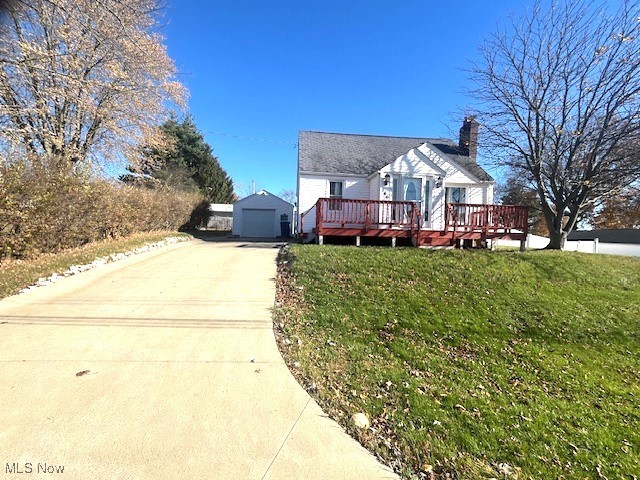 view of front of house with a garage, an outdoor structure, a wooden deck, and a front lawn