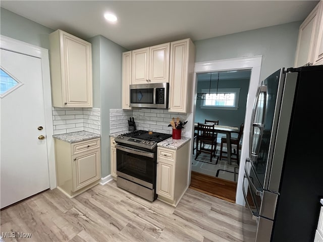 kitchen with tasteful backsplash, light wood-type flooring, light stone counters, and stainless steel appliances