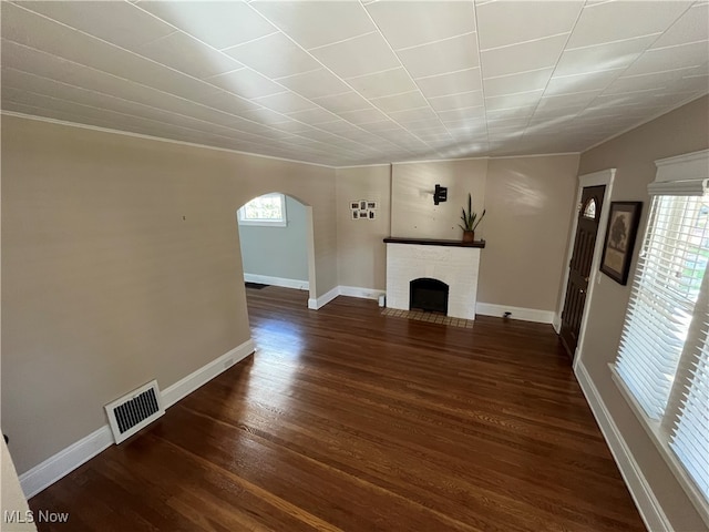 unfurnished living room featuring a brick fireplace and dark hardwood / wood-style flooring