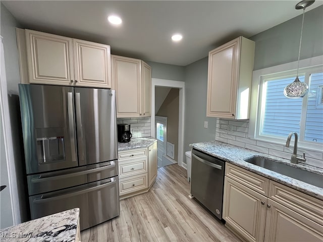 kitchen with stainless steel appliances, hanging light fixtures, sink, tasteful backsplash, and light hardwood / wood-style flooring