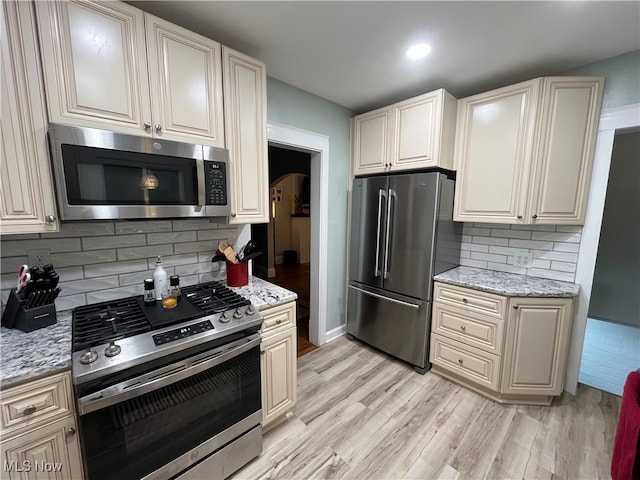 kitchen featuring light hardwood / wood-style floors, light stone countertops, backsplash, and appliances with stainless steel finishes