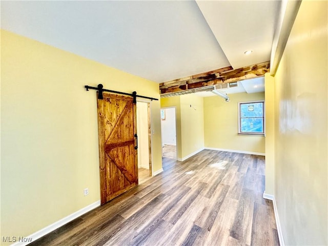 empty room featuring beam ceiling, a barn door, and hardwood / wood-style flooring