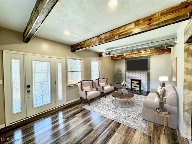 living room featuring a textured ceiling, beam ceiling, dark wood-type flooring, and a brick fireplace