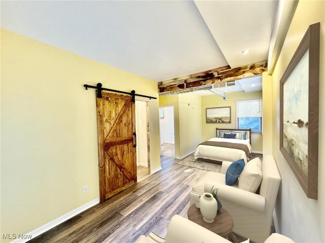 bedroom featuring wood-type flooring, a barn door, and beam ceiling