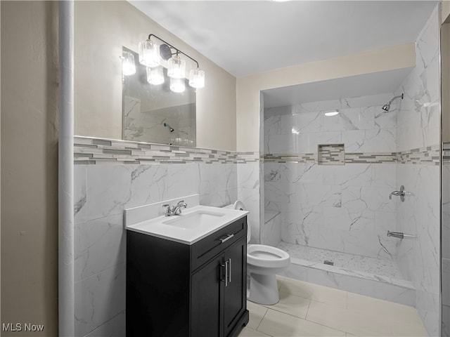 bathroom featuring vanity, toilet, a tile shower, and tile walls