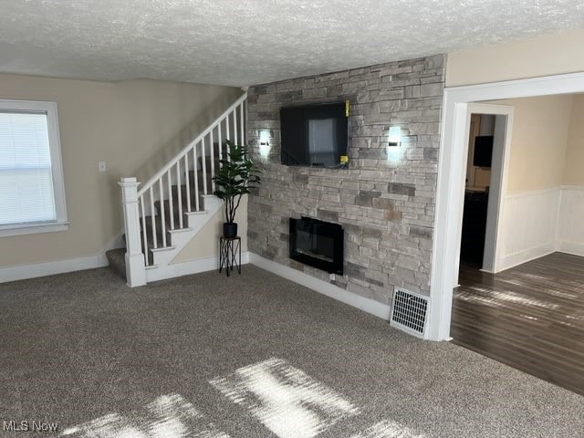 unfurnished living room with a stone fireplace, a textured ceiling, and dark colored carpet