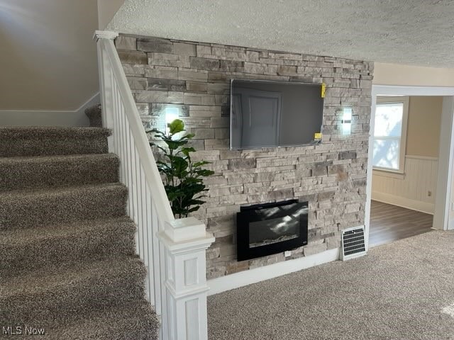 stairway featuring a stone fireplace, wood-type flooring, and a textured ceiling