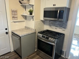 kitchen with stainless steel appliances, white cabinetry, light stone countertops, decorative backsplash, and dark wood-type flooring