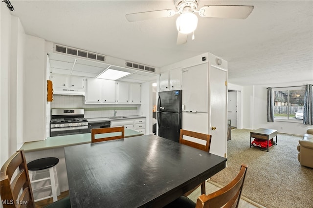 kitchen featuring black fridge, stainless steel gas range oven, decorative backsplash, white cabinets, and ceiling fan