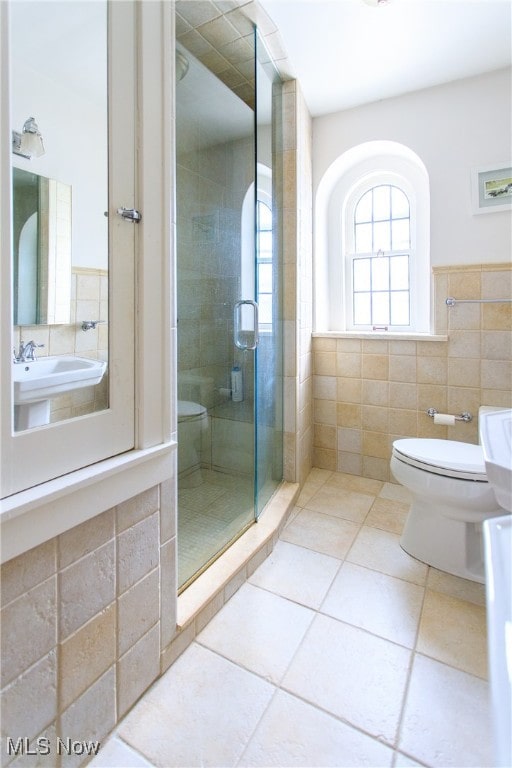 bathroom with tile walls, tile patterned flooring, toilet, and a shower with door