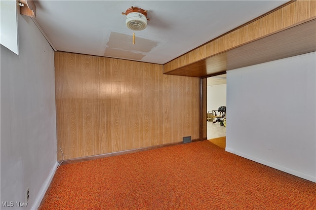 carpeted spare room featuring wood walls