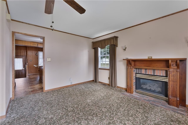 unfurnished living room featuring dark colored carpet, wooden walls, ceiling fan, and crown molding