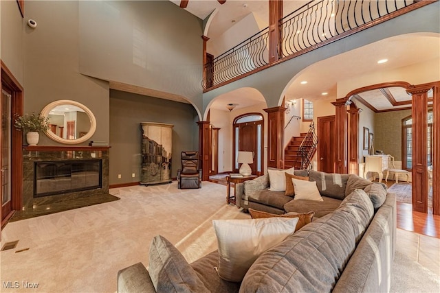 living room featuring decorative columns, light carpet, a high end fireplace, and a high ceiling