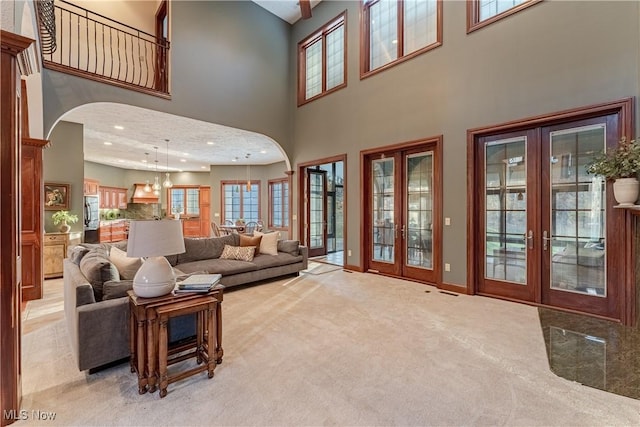 living room with light carpet, french doors, a towering ceiling, and a notable chandelier