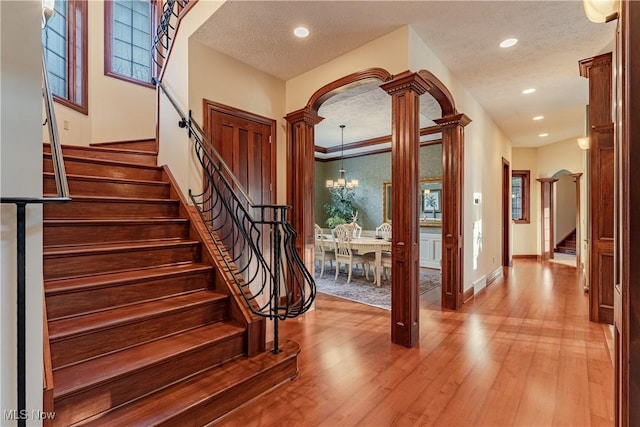 interior space featuring decorative columns, hardwood / wood-style flooring, ornamental molding, a textured ceiling, and a chandelier